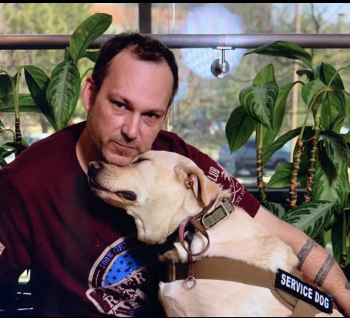 A man and his dog are sitting in front of some plants.