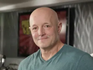 A bald man with a shaved head and a green shirt.