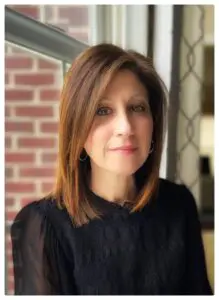 A woman with long hair wearing black is standing outside.