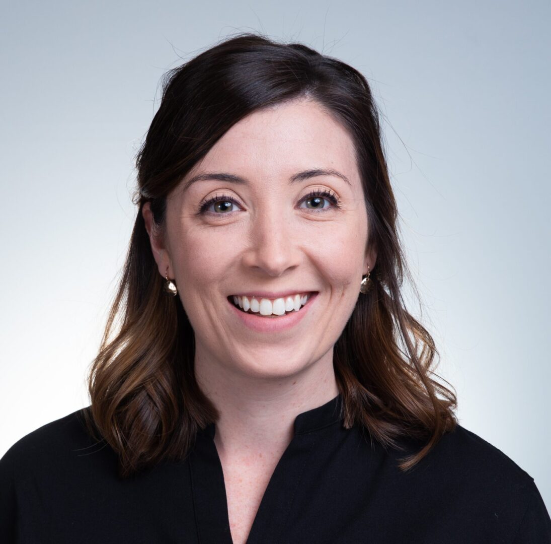 A woman with long hair and wearing black is smiling.